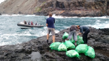 Cleaning up the plastic trash from the remote beach at Sharks Valley on St Helena. Bagged rubbish roped out to a boat to transport it back to Jamestown.